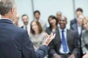 Mature male leader speaking during conference with blurred audience